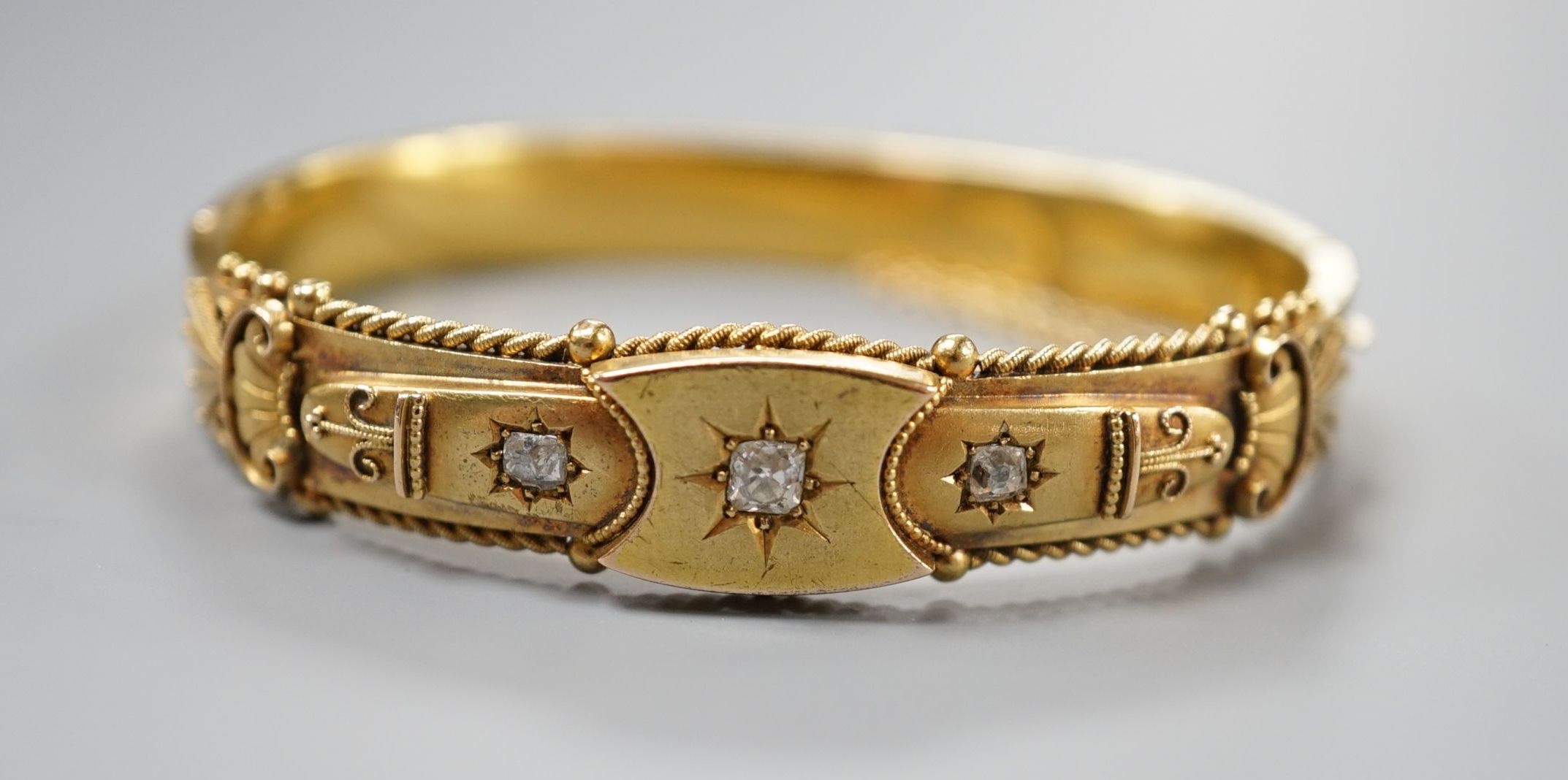 An Edwardian 15ct gold and three stone diamond set hinged bangle, interior diameter 57mm, gross weight 15.8 grams.